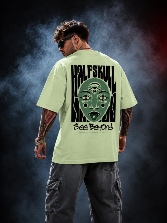 Man wearing the pastel green Half Skull Beyond Vision oversized T-shirt with the many eyed face and See Beyond back print